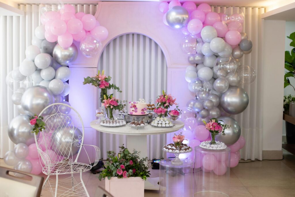 Beautiful birthday celebration setup with pink and silver balloons, floral arrangements, and a stylish cake display.